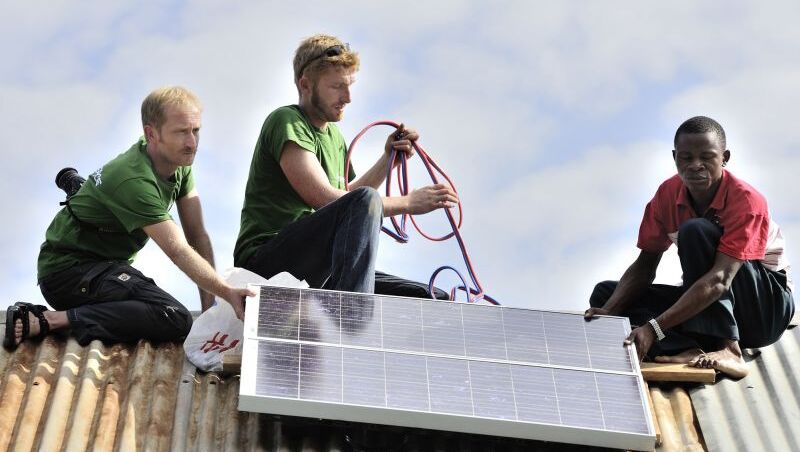 Drei Männer installieren ein Solarpanel auf einem Dach,